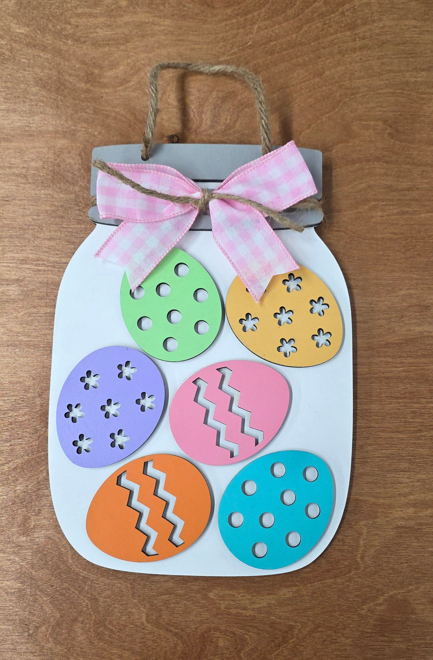 Decorative Easter egg sign with colorful eggs and a pink bow on a wooden surface