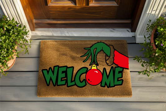 Doormat with a cartoon hand holding a ornament and the word 'Welcome' on a wooden floor.