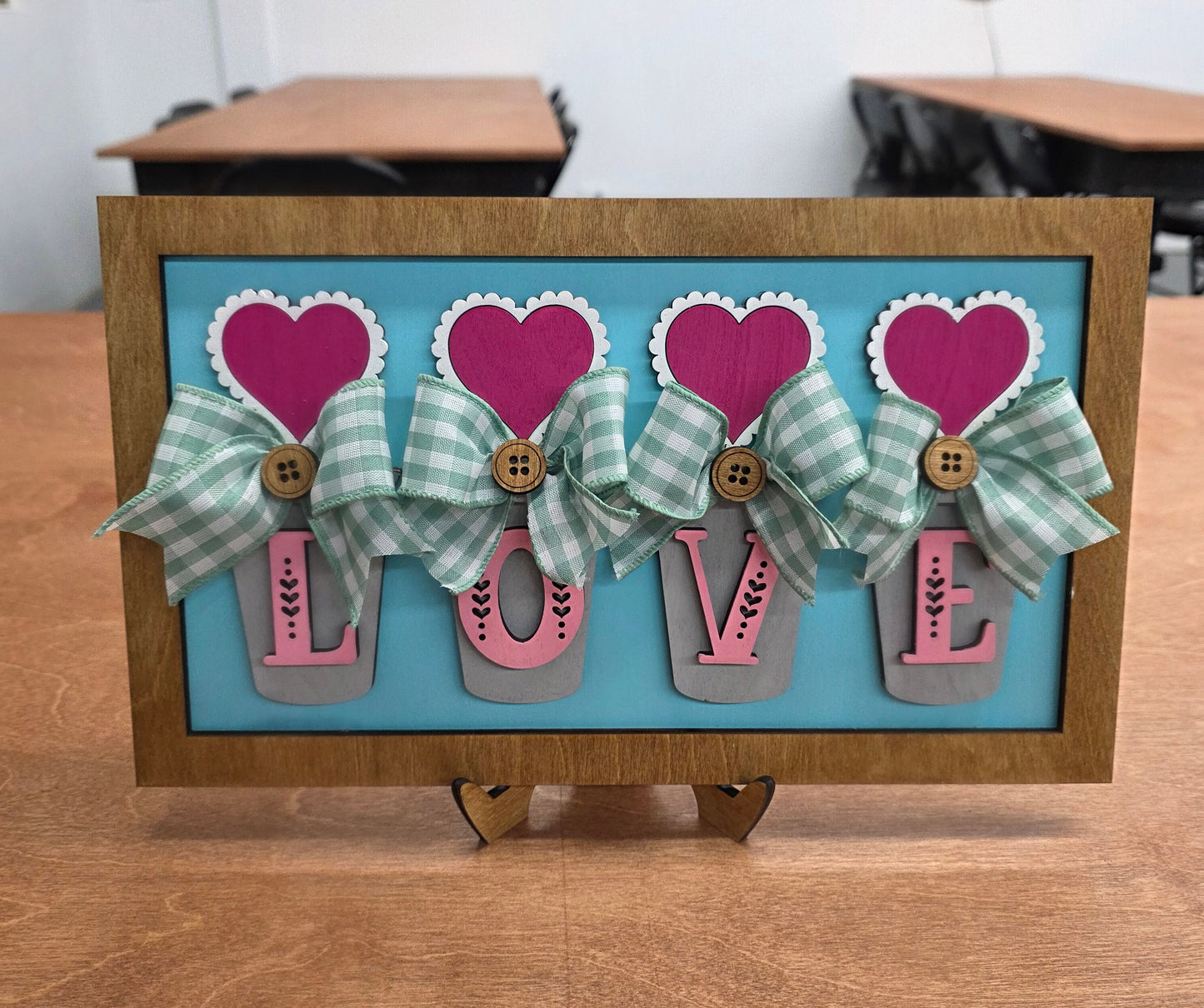 Decorative wall art with heart and arrow designs on a blue background, framed in brown.